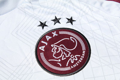 Een wit Ajaxlogo op een donkerrode badge met zwarte omlijning. © Ajax Life